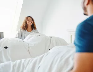 Couple changing bedding at home and placing comforter on top of bed.