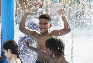 Young child laughing and smiling with friends as they play in a water park in the summer.