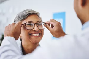 A doctor helping a patient try on and adjust their new glasses during an ophthalmology appointment.