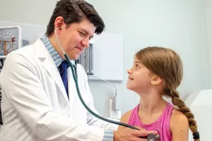 James Goodman, MD of Circle Health and Pelham Family Practice listening to a pediatric patient's heart with a stethoscope during a primary care appointment.